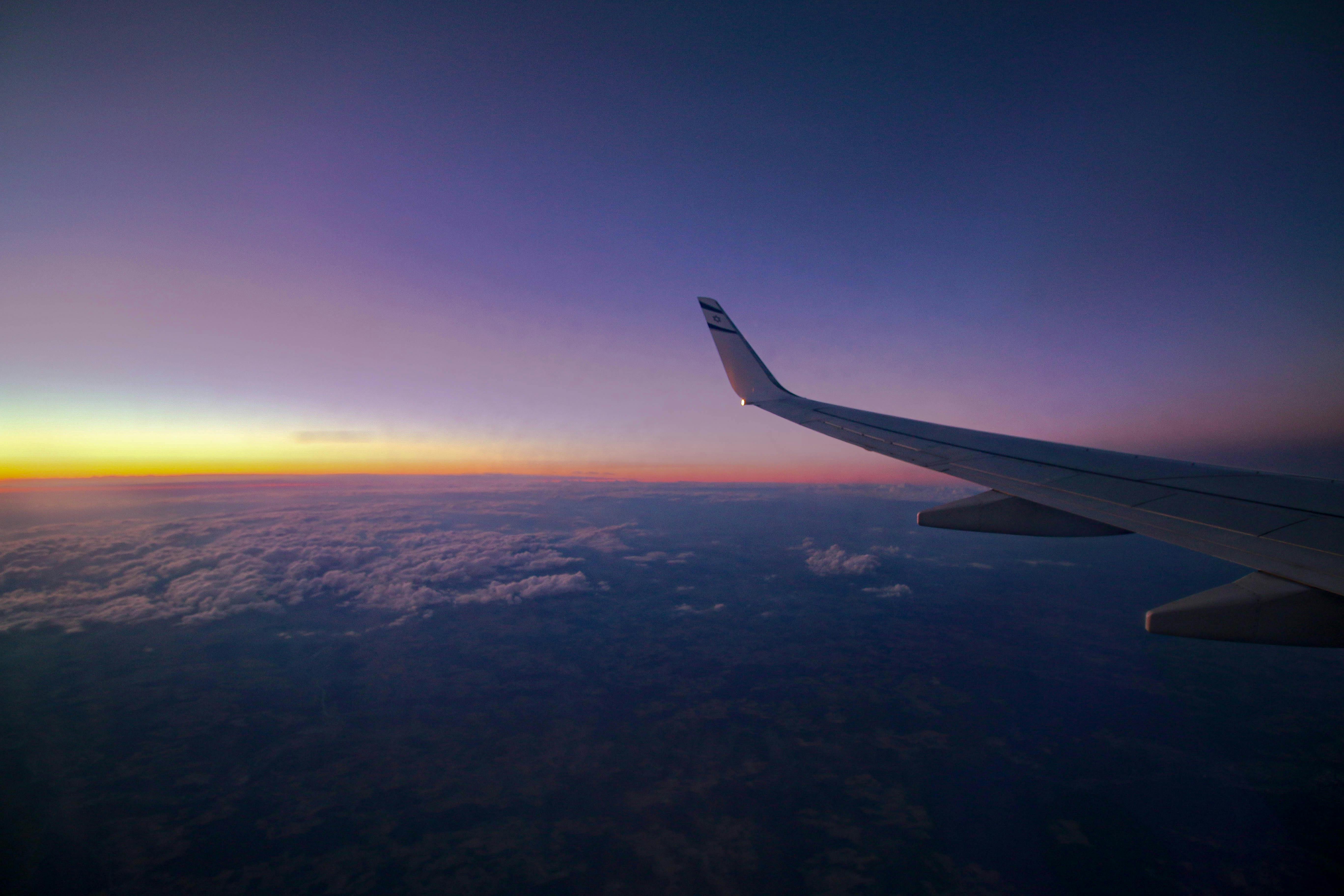 נוף מחלון מטוס מעל עננים בשמי דמדומים סגולים | View from Airplane Window over Clouds in Purple Twilight Sky