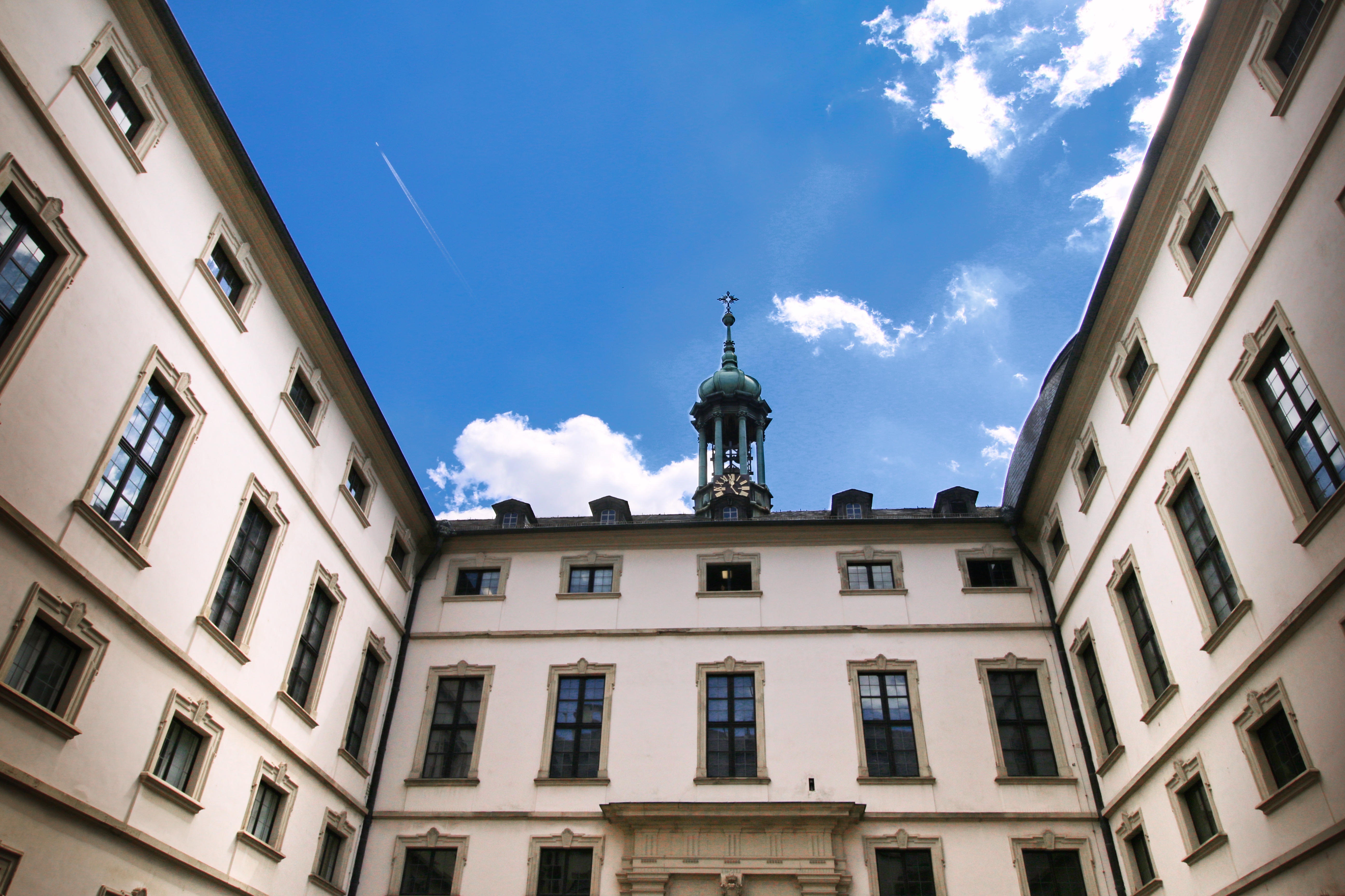 חצר פנימית של מבנה היסטורי לבן עם מגדל שעון תחת שמיים כחולים | Inner Courtyard of a White Historic Building with a Clock Tower under Blue Skies