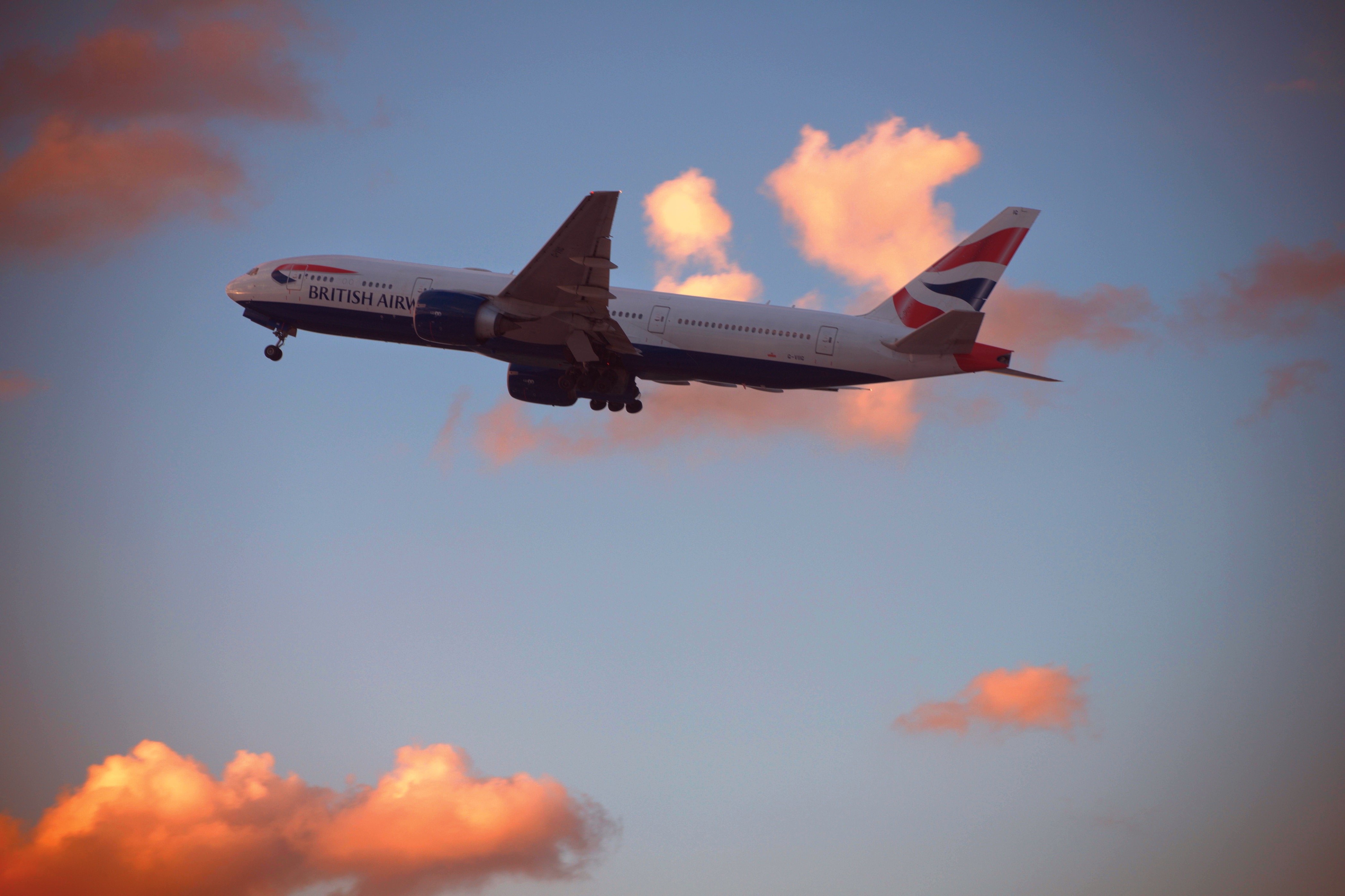 מטוס נוסעים של בריטיש איירווייז בטיסה בשמי שקיעה עם עננים מוארים | British Airways Passenger Jet in Flight in Sunset Skies with Illuminated Clouds