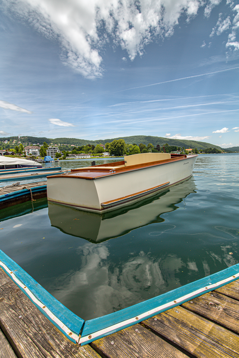סירת מנוע קלאסית מעץ עוגנת במזח באגם תחת שמיים כחולים | Classic Wooden Motorboat Moored at a Lake Dock Under Blue Sky