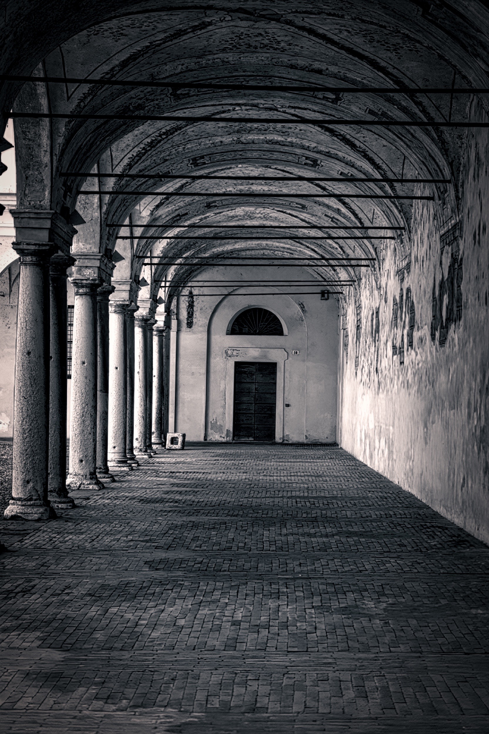 מבט עומק לאורך מעבר עמודים (ארקדה) עתיק ומרוצף עם קשתות ודלת
