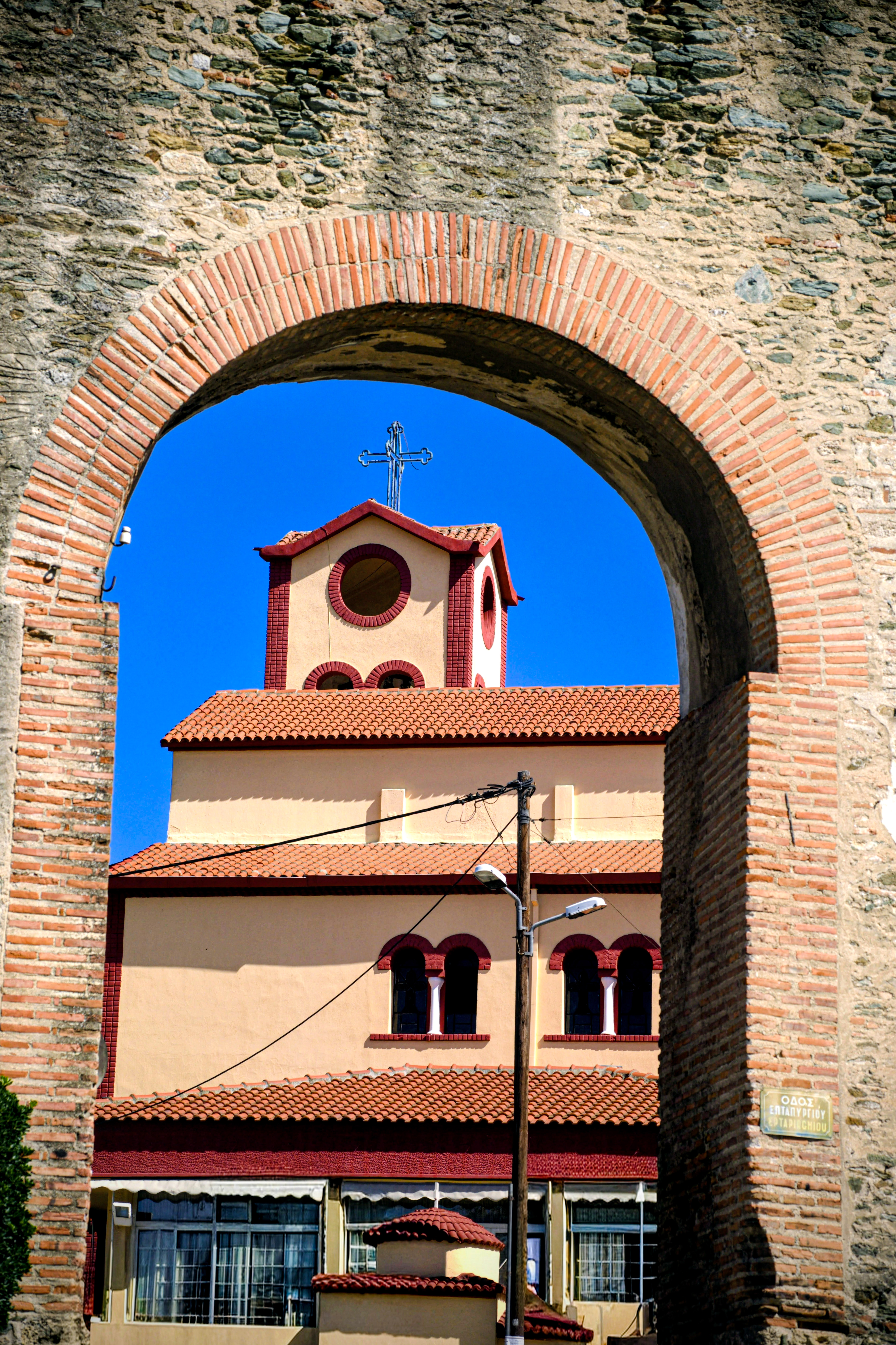 כנסייה עם גג רעפים אדומים ממוסגרת מבעד לקשת אבן עתיקה מלבנים