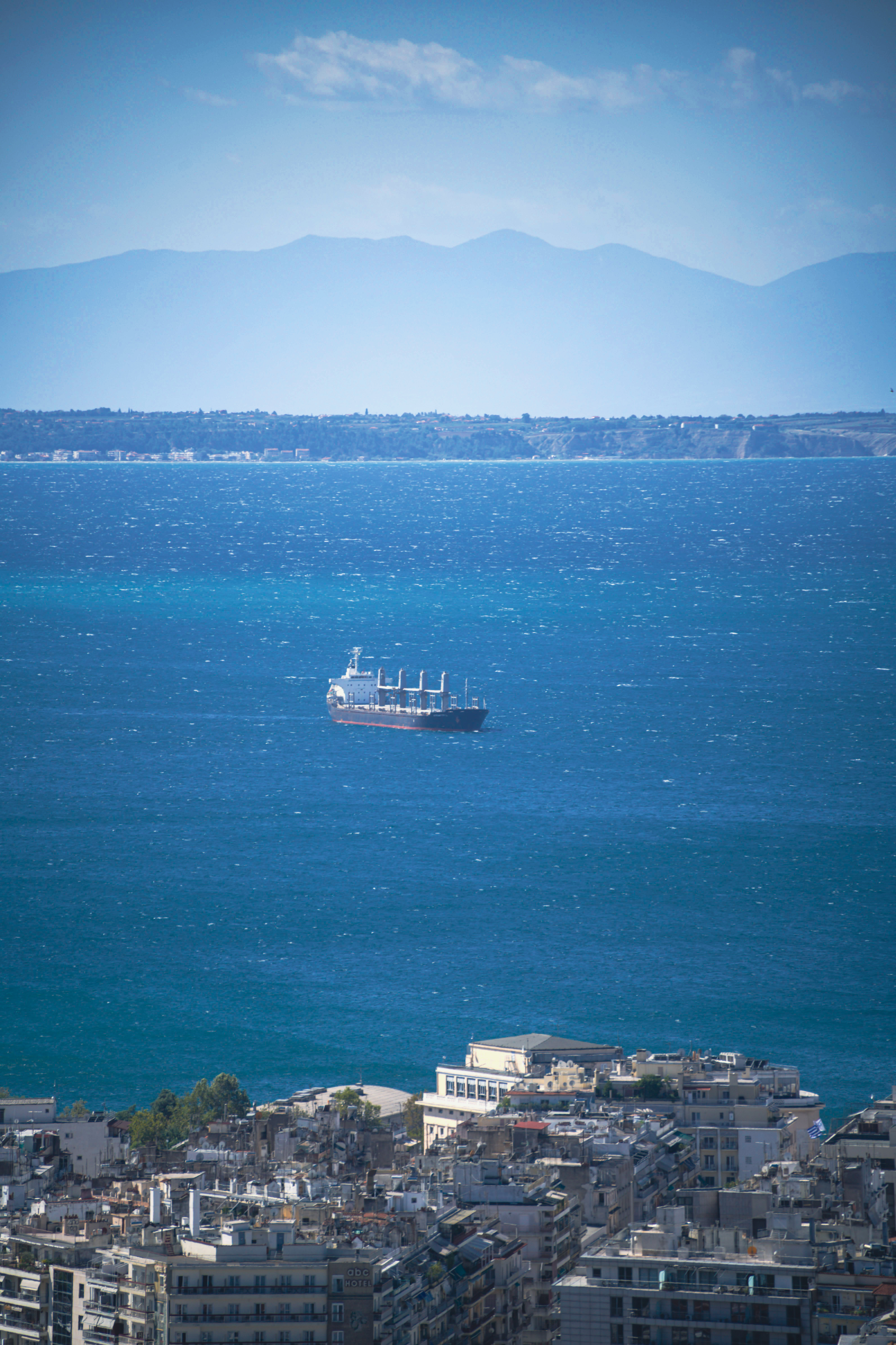 נוף עירוני של עיר חוף עם ספינת משא בים הכחול והרים באופק