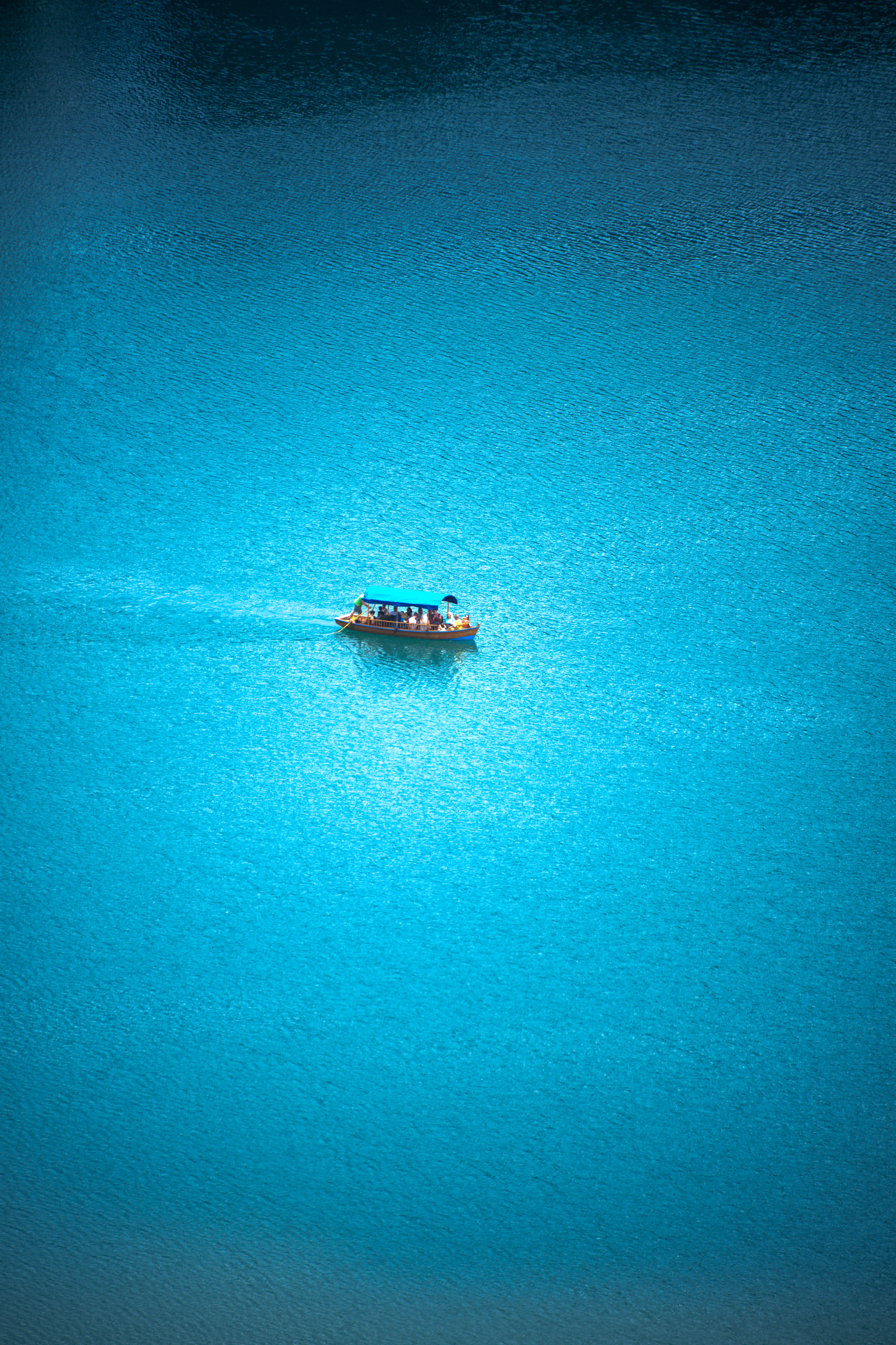 צילום אווירי מינימליסטי של סירה קטנה שטה בלב גוף מים כחול וצלול