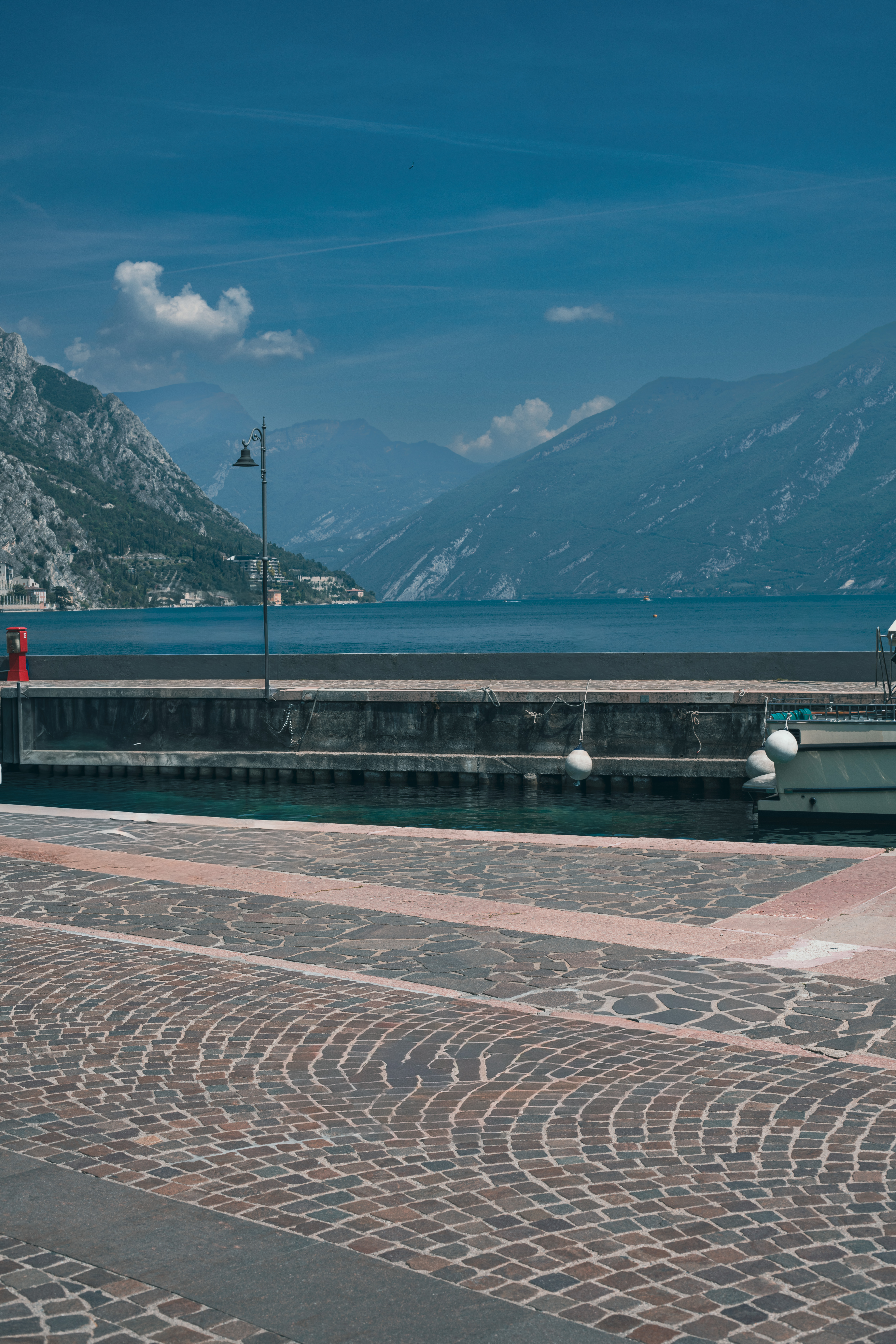 טיילת מרוצפת אבן על שפת אגם אלפיני כחול למרגלות הרים נישאים